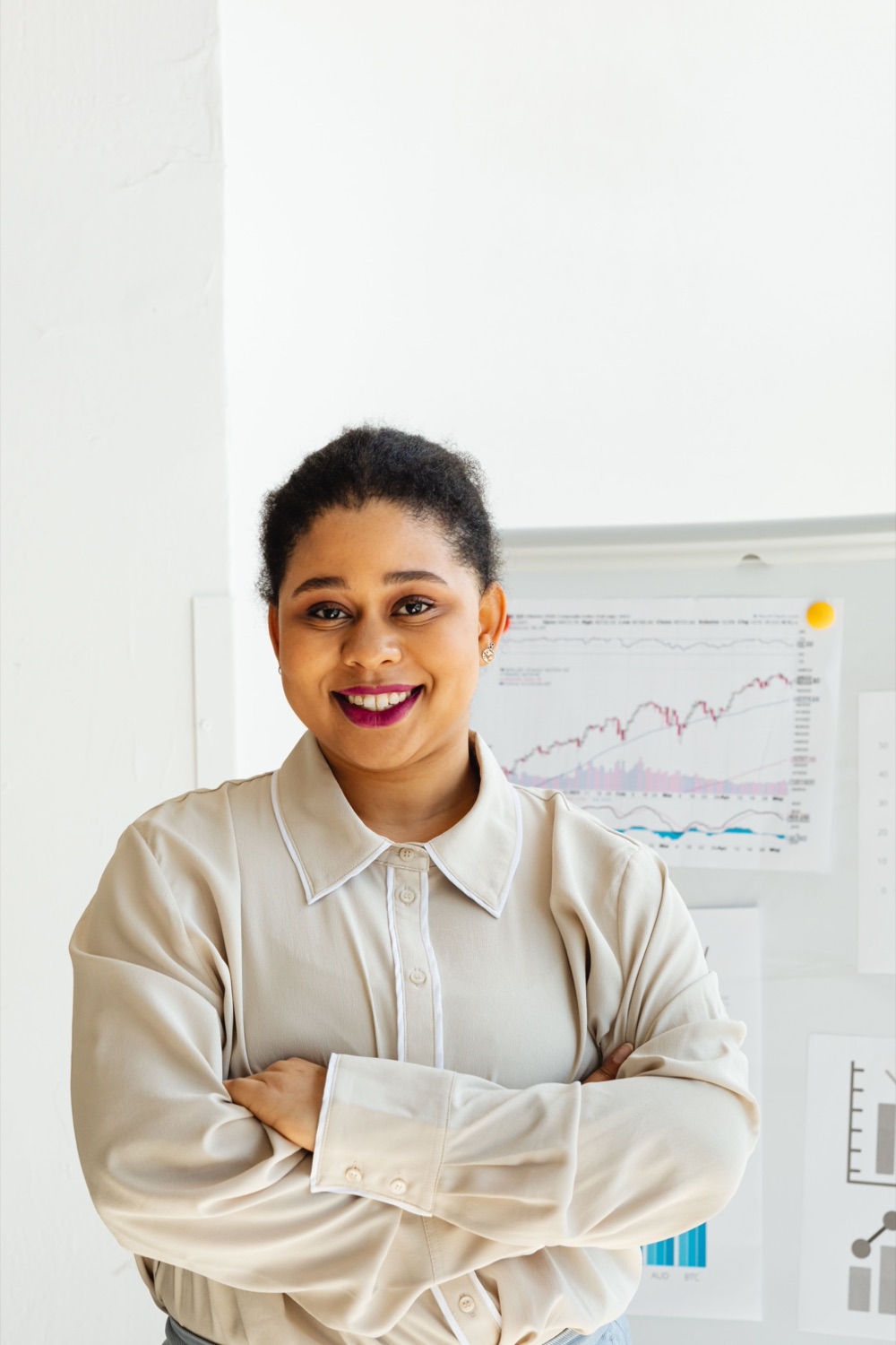 A smiling business owner, arms folded, in front of her sales charts